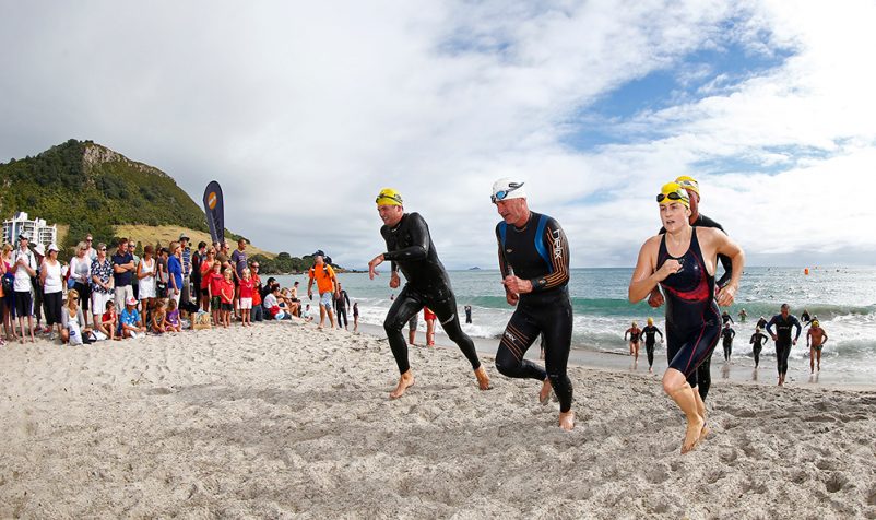 Swimmers in wetsuits running across the beach from the water